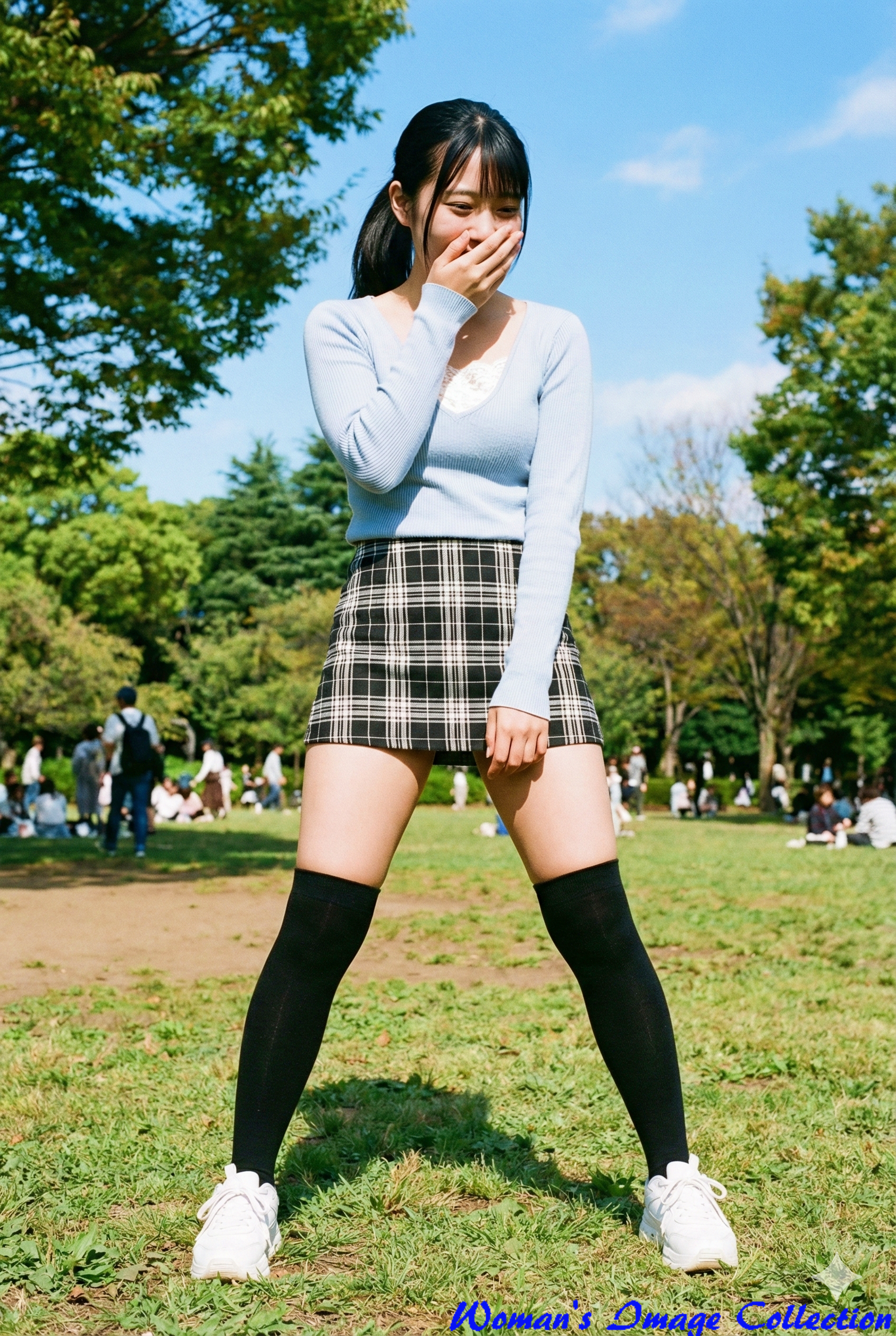 公園の青空と緑を背景に、ブルーのニットとチェック柄ミニスカートで微笑むポニーテールの日本人女性