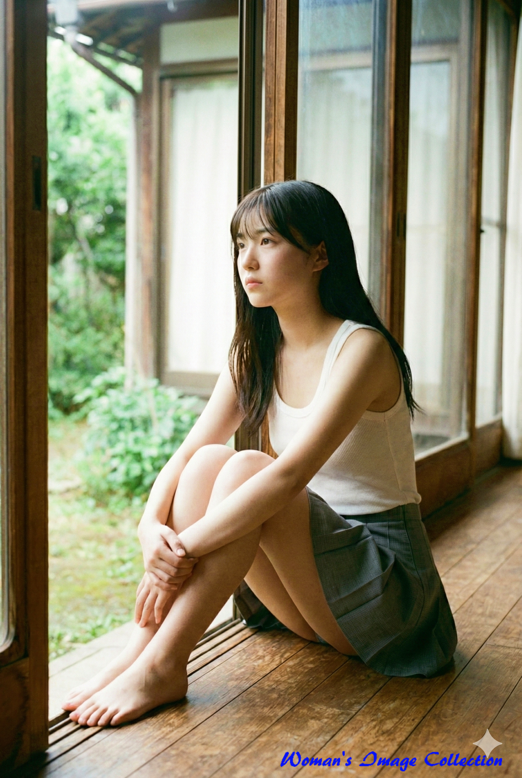 縁側に体育座りで座り、外を眺める女性。物憂げな表情と柔らかな自然光。